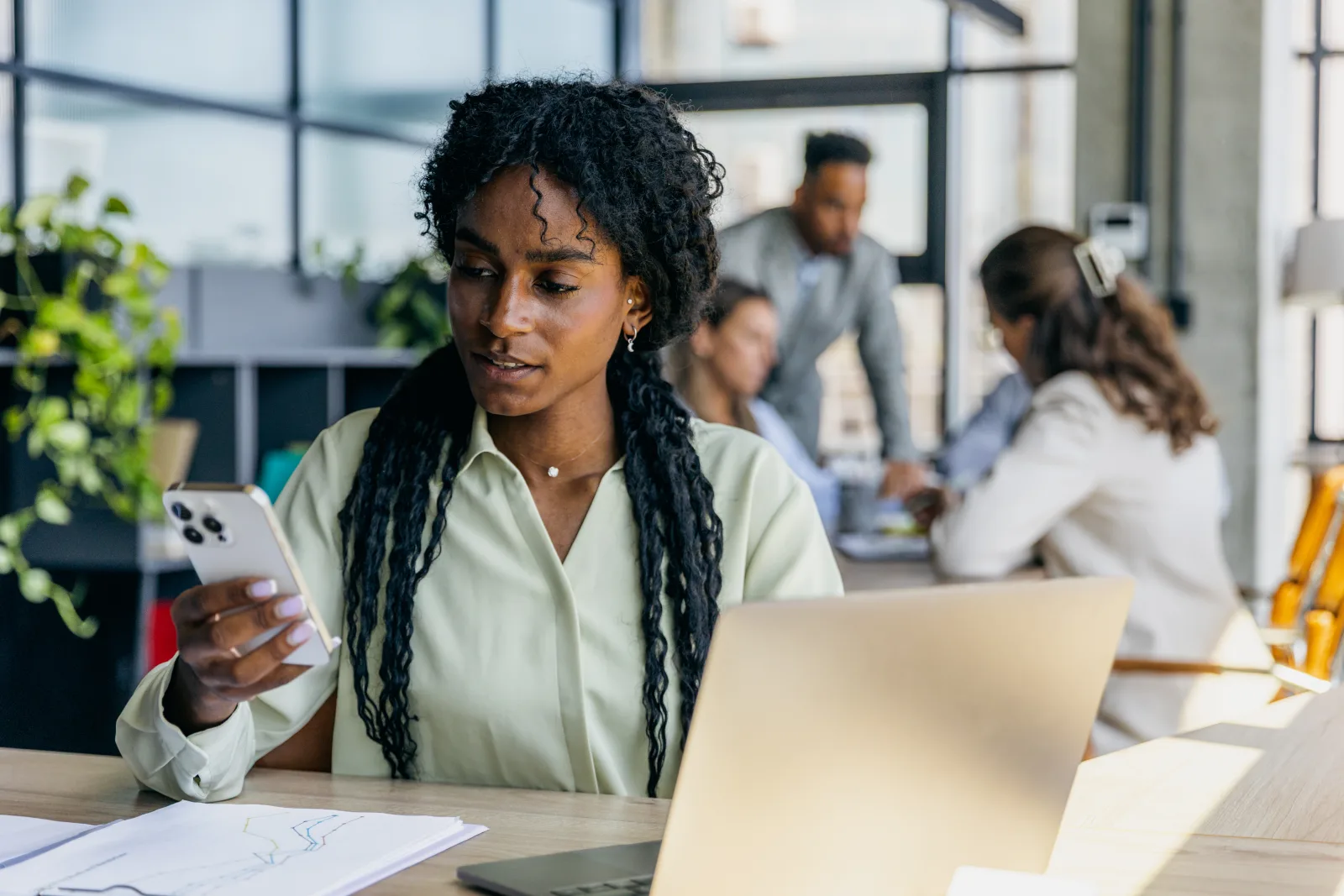 Una professionista del marketing controlla lo smartphone davanti al laptop nell'ufficio di un'agenzia